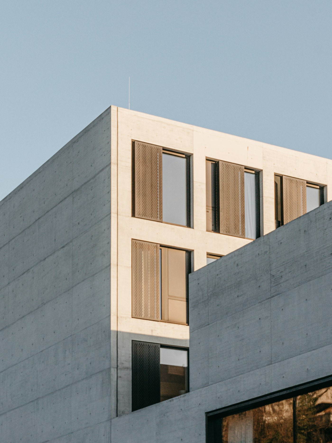 Concrete building with bronze shutters lit by low evening sun
