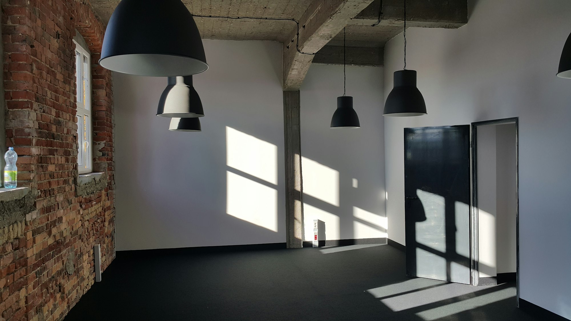 Sunlight falling across a white wall under pendant lights in an empty office