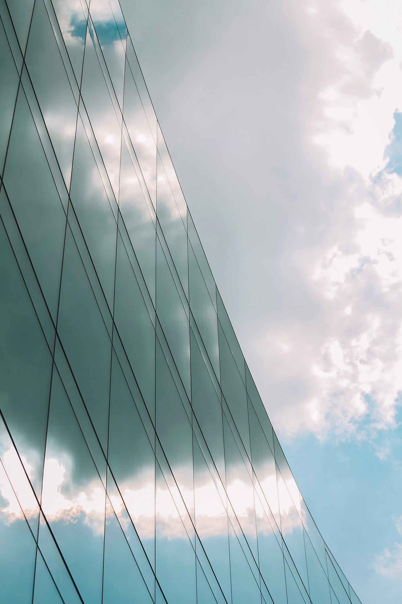 A curved glass facade reflecting white clouds and pale blue sky